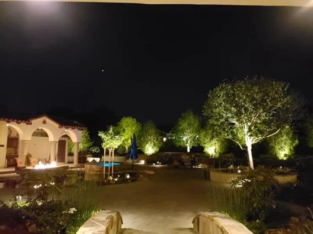 Elegant night garden with lit trees, pool, and cozy seating area. Serene outdoor retreat.