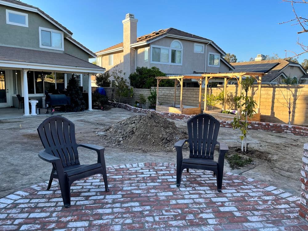 Adirondack chairs on a brick patio in a residential backyard with construction.