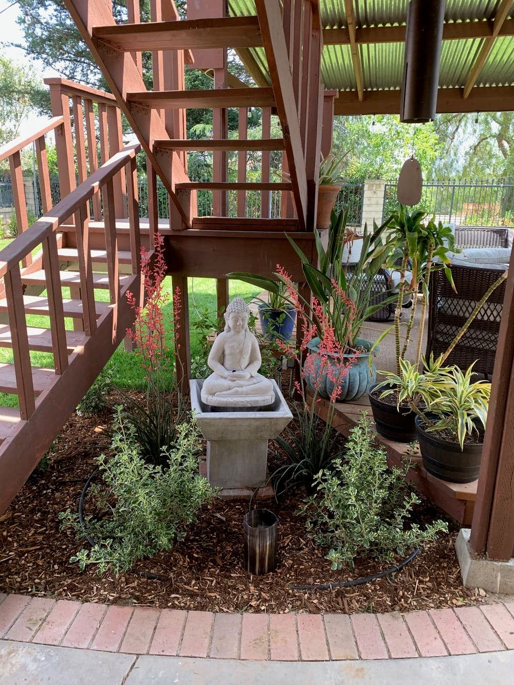 Serene outdoor space with Buddha statue, plants, and wooden stairs, creating a peaceful retreat.