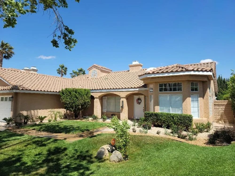 Desert-style home with tiled roof and lush landscaping under a clear blue sky.
