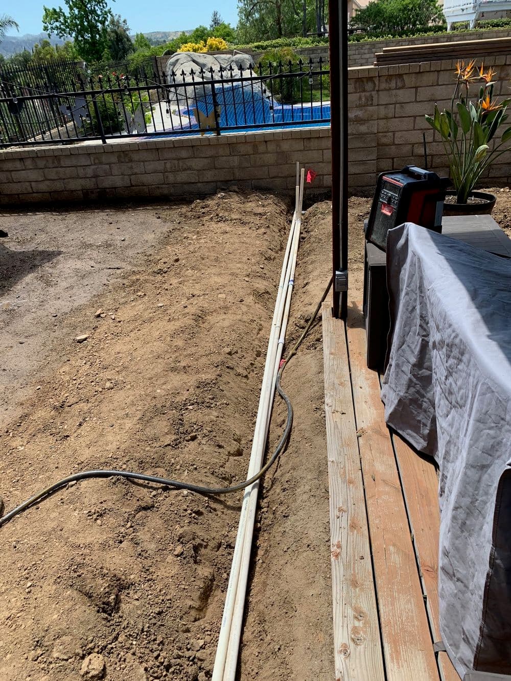 Construction site showing trench, electric cables, and outdoor landscape with pool and plants.