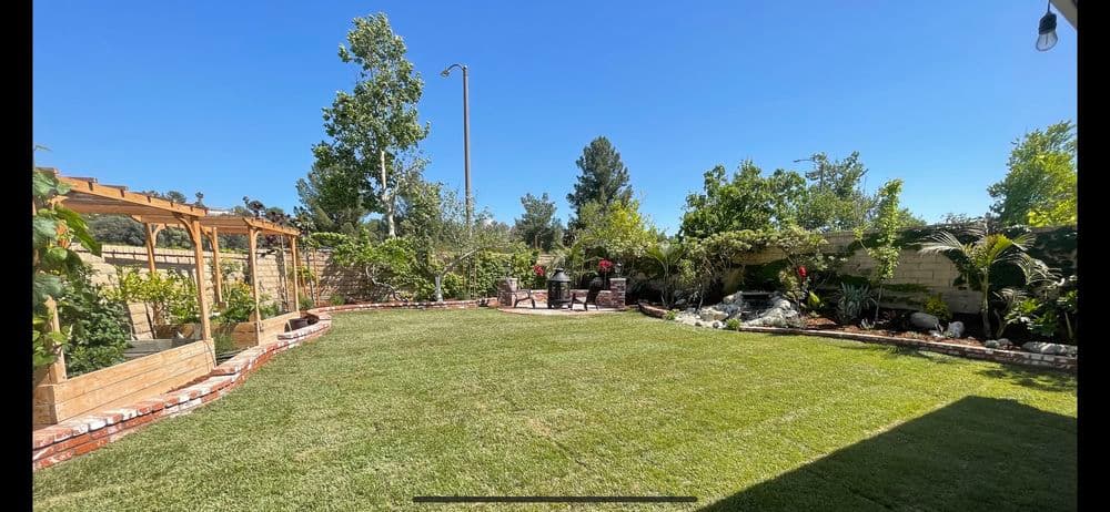 Lush backyard with green lawn, seating area, and landscaped garden under clear blue sky.