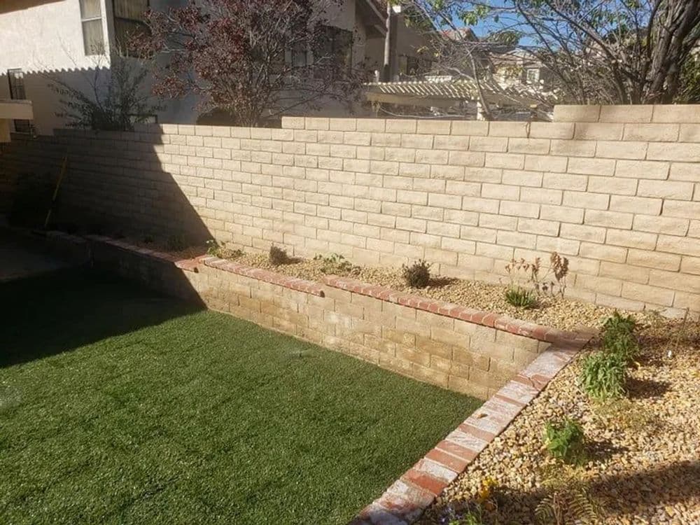 Landscaped backyard featuring a stone wall, raised beds, and artificial grass.