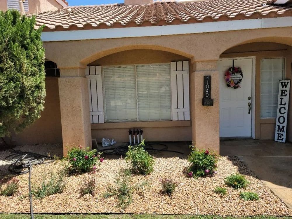 Desert-style home exterior with plants, welcome sign, and decorative window shutters.