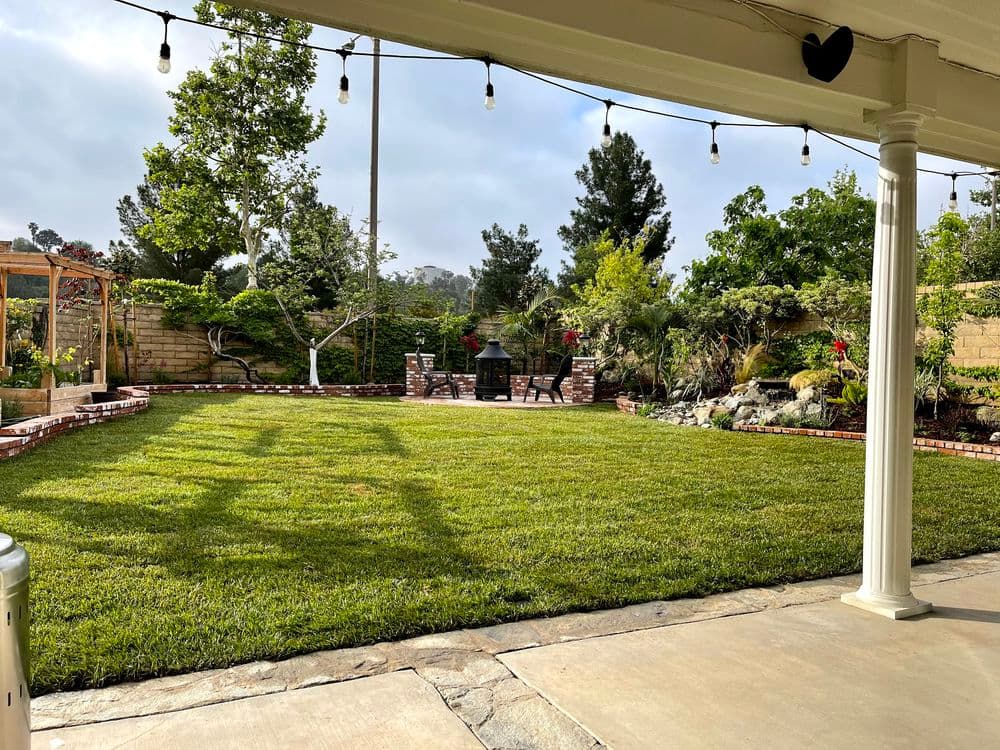Lush green backyard with garden seating, pathways, and decorative landscaping under string lights.