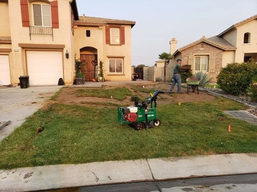 Lawn renovation in progress with a man using a tiller in front of a suburban house.