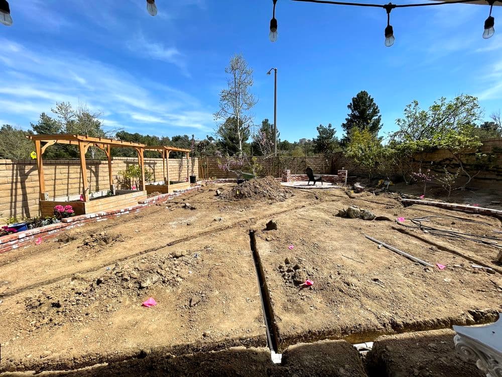 Bare yard undergoing landscaping with marked areas and wooden structures under a clear blue sky.