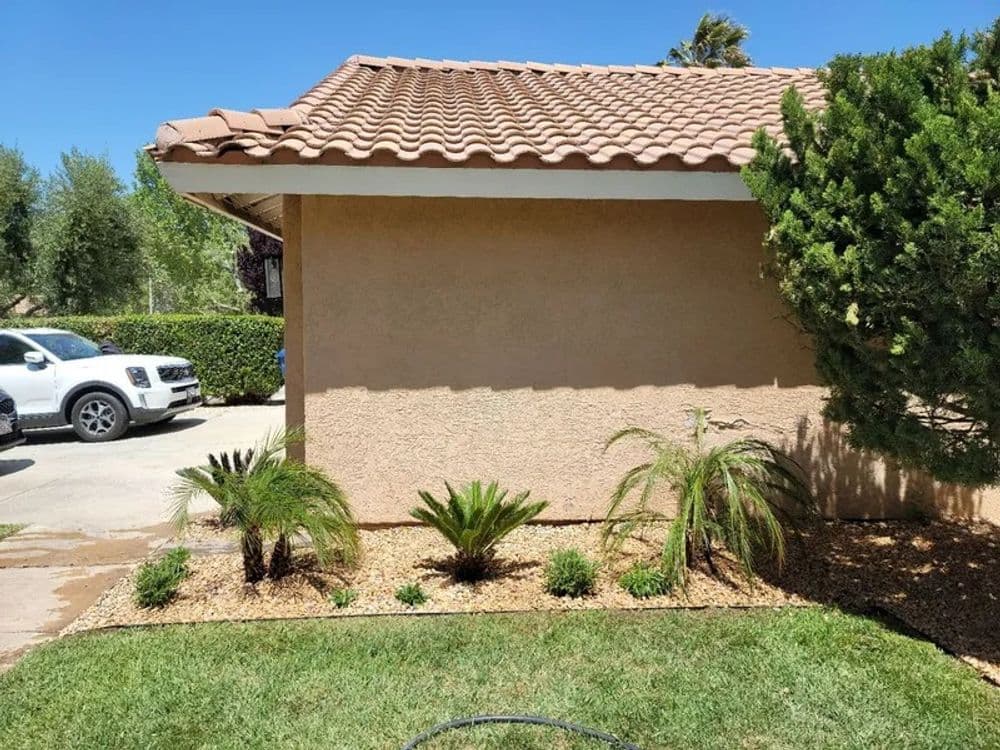 Residential exterior featuring a tan house, palm plants, and gravel landscaping. Bright sunny day.