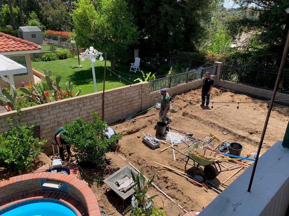 Landscaping crew working in a residential yard with tools, plants, and a pool.