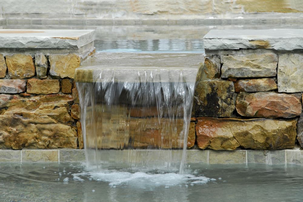 Waterfall cascading over stone wall in a serene outdoor setting. Relaxing natural feature.