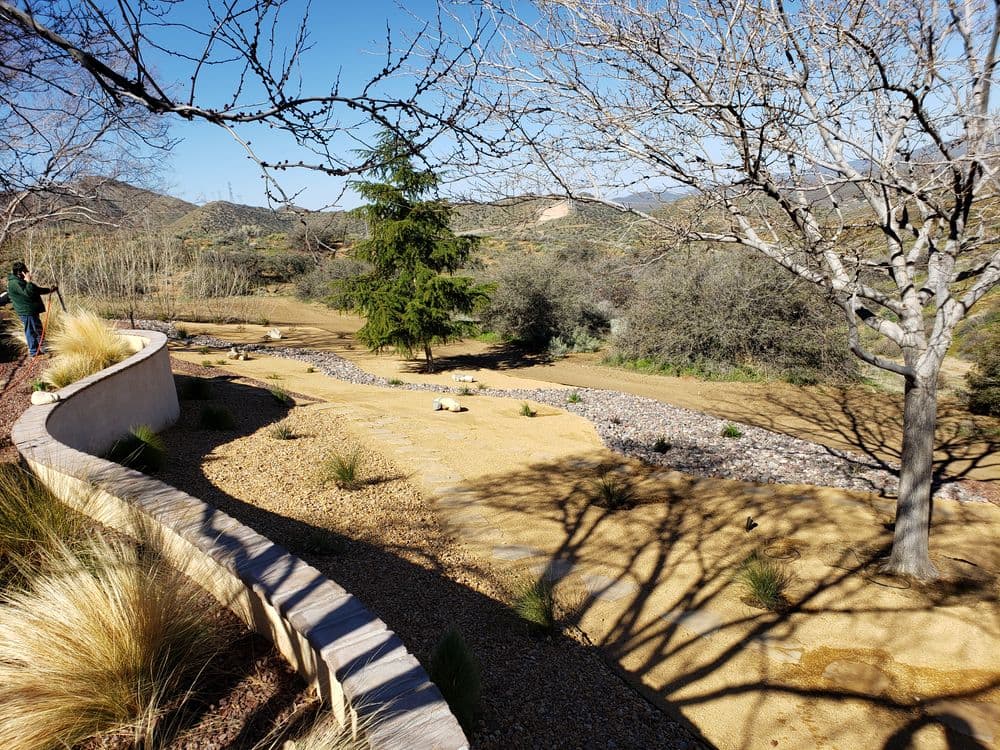 Landscape view featuring a winding path, bare trees, and a rocky creek in a serene outdoor setting.