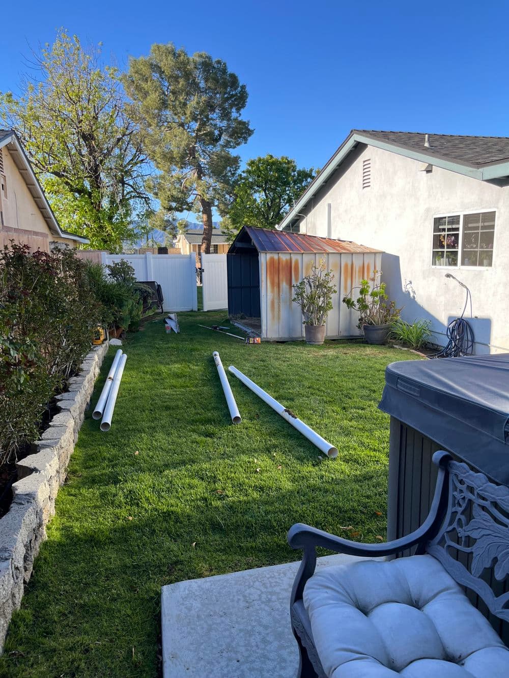 Backyard scene featuring a metal shed, PVC pipes on grass, and a residential home.