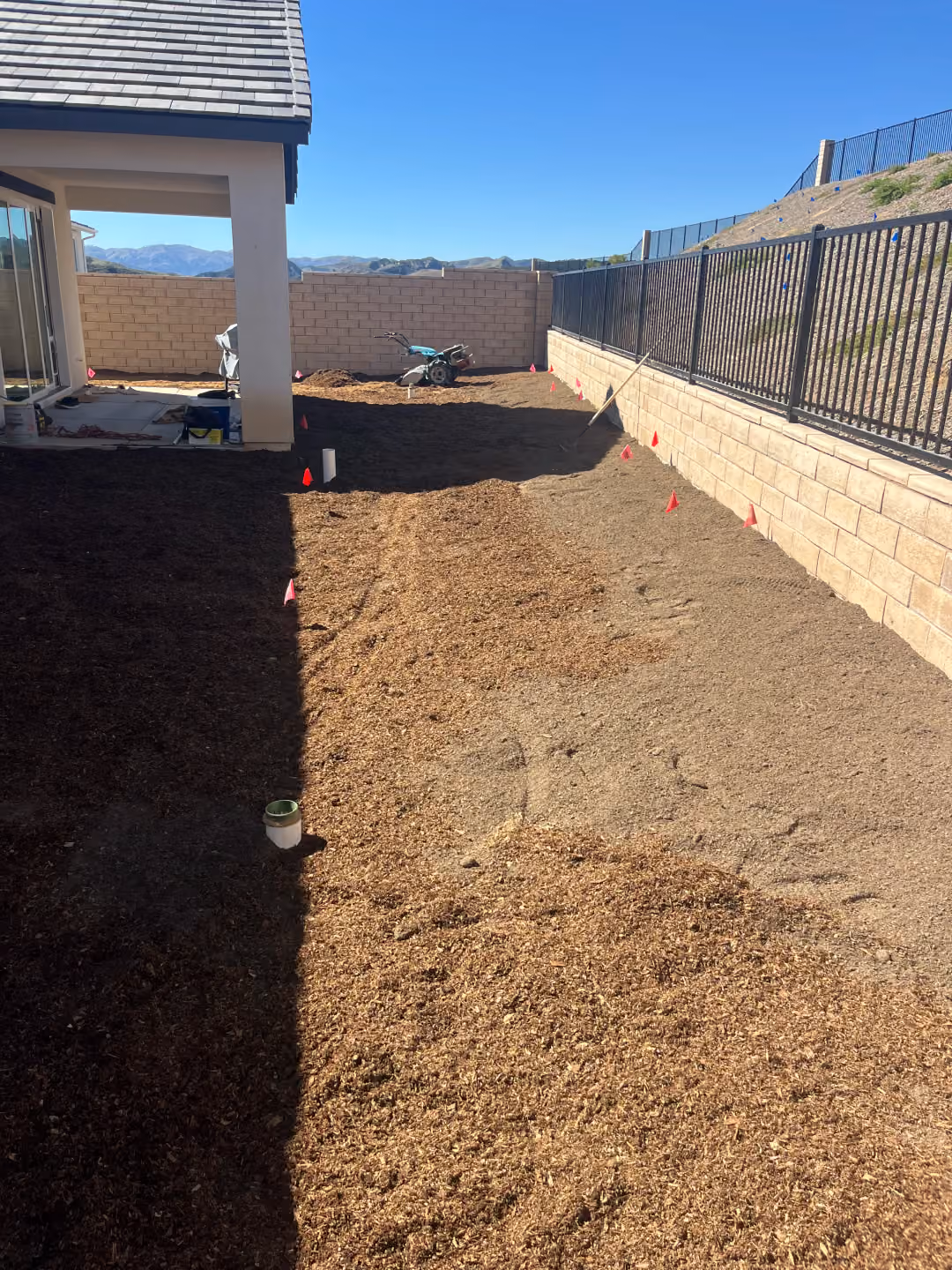 Backyard scene showing dirt and mulch being prepared for the installation of a new patio.