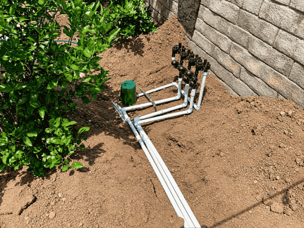 A garden hose connected to a metal pipe, lying on a grassy surface in a garden setting.